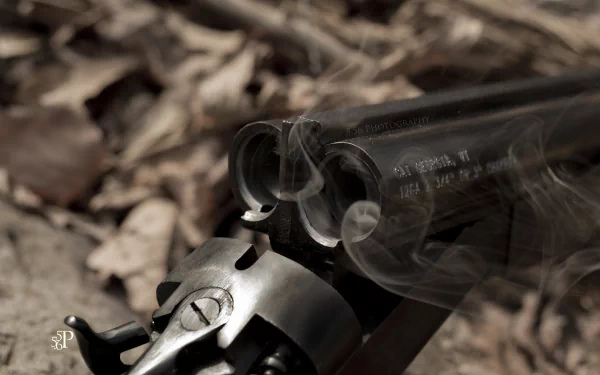 Close-up of a man-made shotgun barrel releasing smoke, captured in 4K Ultra HD as a PC desktop wallpaper with a blurred natural background.