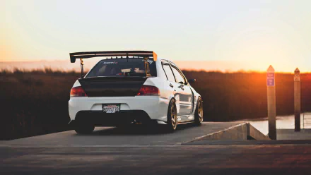 A Mitsubishi Lancer Evolution parked on a scenic overlook at sunset, showcasing its sleek design and sporty rear wing, captured in high-definition for desktop wallpaper.