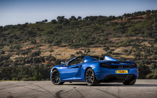 Blue McLaren MP4-12C vehicle, rear three-quarter view on a roadside with rolling hills — 2K Quad HD PC desktop wallpaper/background.