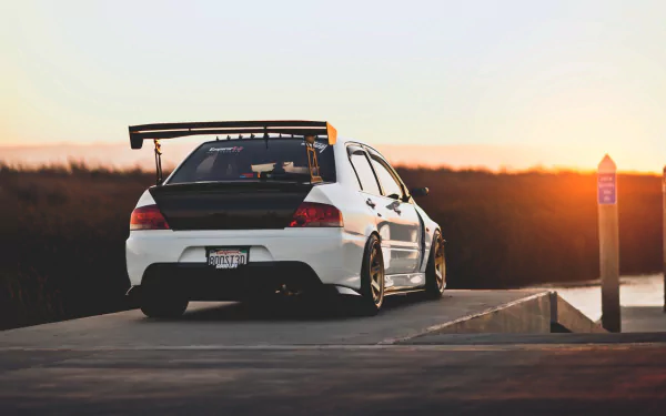 A Mitsubishi Lancer Evolution parked on a scenic overlook at sunset, showcasing its sleek design and sporty rear wing, captured in high-definition for desktop wallpaper.