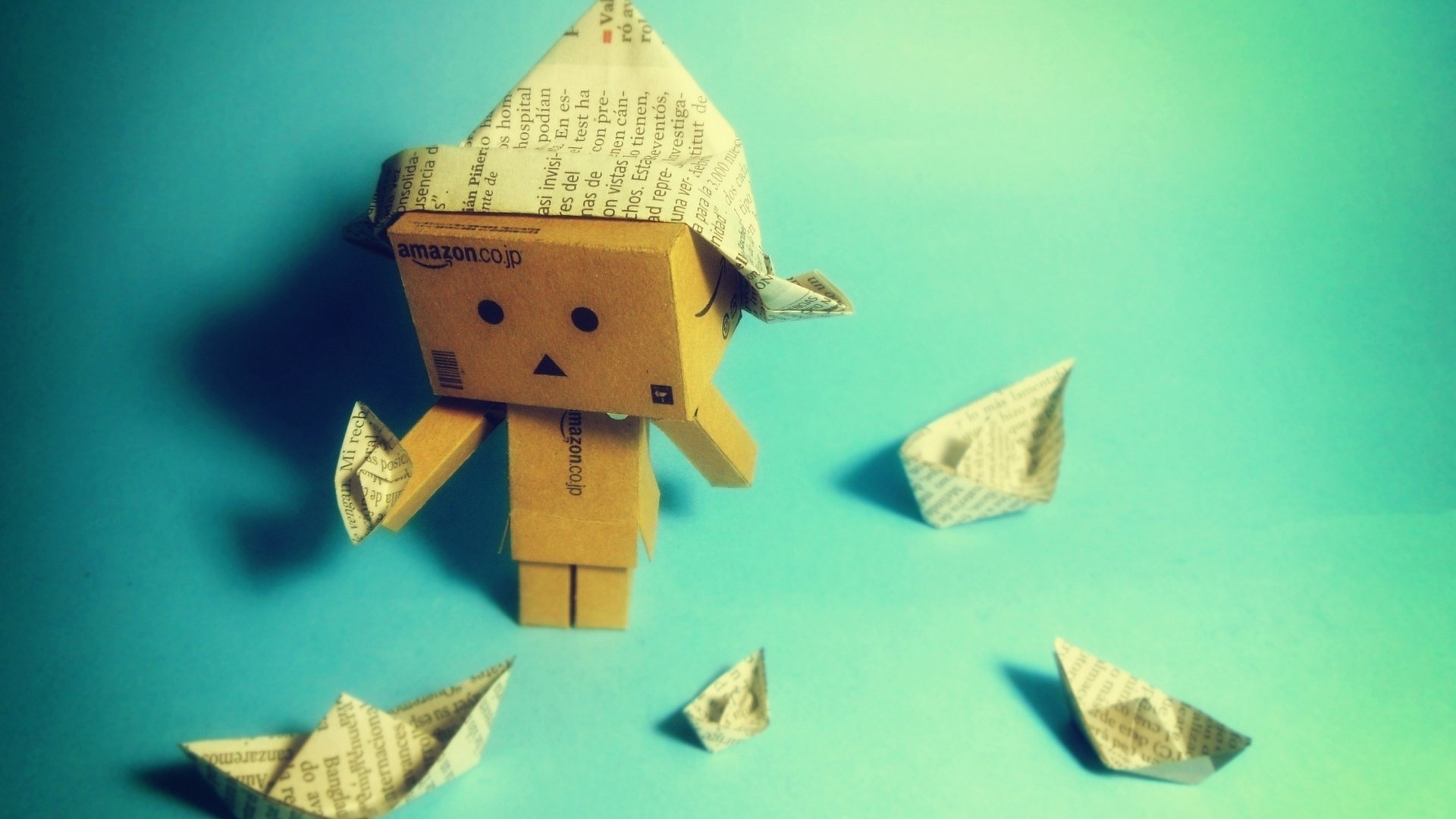 HD PC desktop wallpaper: Danbo cardboard figure wearing a newspaper hat, holding a paper boat, surrounded by origami boats on a turquoise background.