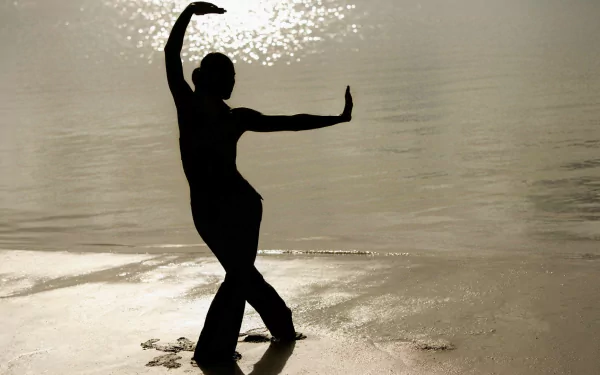 A silhouette of a woman practicing yoga by the water, with sunlight reflecting on the surface, creating a tranquil beach scene. This HD desktop wallpaper enhances any background.