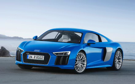 A stunning blue Audi R8 V10 stands elegantly by the shore, showcasing its sleek design and powerful presence, making it a striking HD desktop wallpaper.