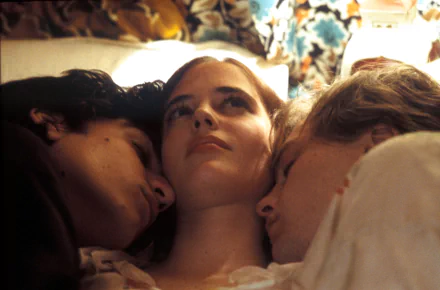 HD PC desktop wallpaper: intimate movie still of three young adults lying close in bed; a central woman gazes upward while two companions rest their heads against her shoulders.