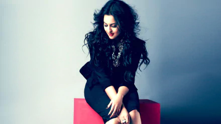 HD wallpaper featuring Sonakshi Sinha, showcasing her stylish look with dark, wavy hair and an elegant outfit, exuding confidence and charm against a muted background.