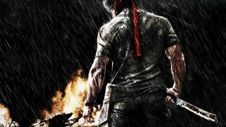 HD desktop wallpaper featuring Rambo from the movie Rambo, showcasing a rugged image of the character in action, with a red bandana, holding a weapon, and standing in the rain against a fiery background.