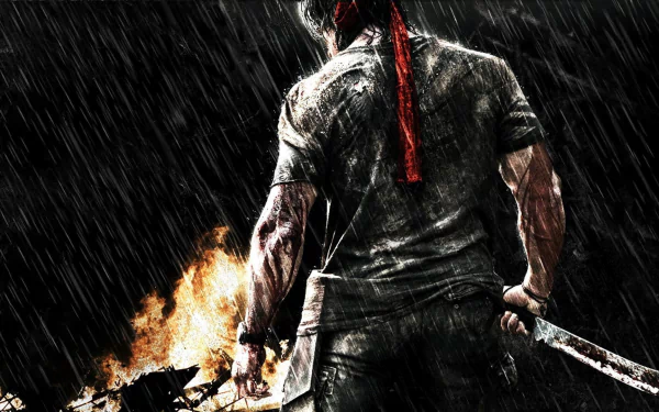 HD desktop wallpaper featuring Rambo from the movie Rambo, showcasing a rugged image of the character in action, with a red bandana, holding a weapon, and standing in the rain against a fiery background.