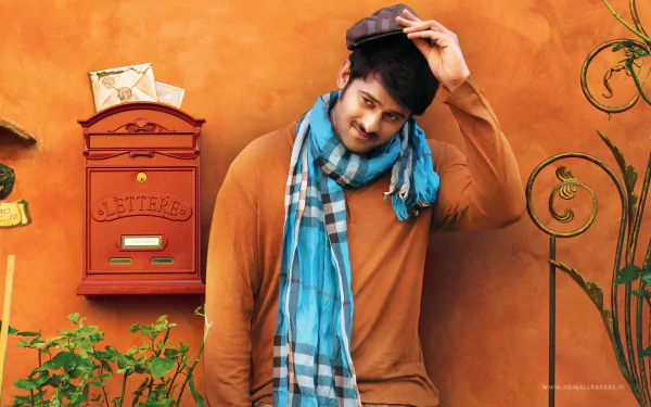 HD PC desktop wallpaper featuring celebrity Prabhas in a casual pose against an orange background with a vintage mailbox and greenery.