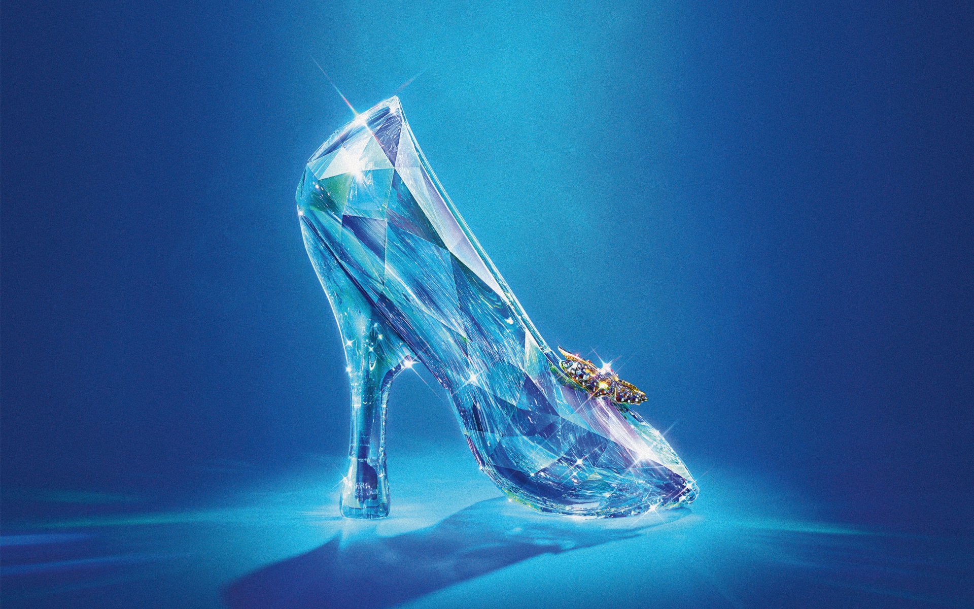 A shimmering glass slipper from the movie Cinderella (2015) glimmers against a blue backdrop, showcasing its intricate design and magical allure as a desktop wallpaper.