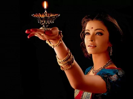 HD desktop wallpaper featuring Bollywood celebrity Aishwarya Rai, elegantly dressed in traditional attire, holding a beautifully ornate lamp against a dark background.