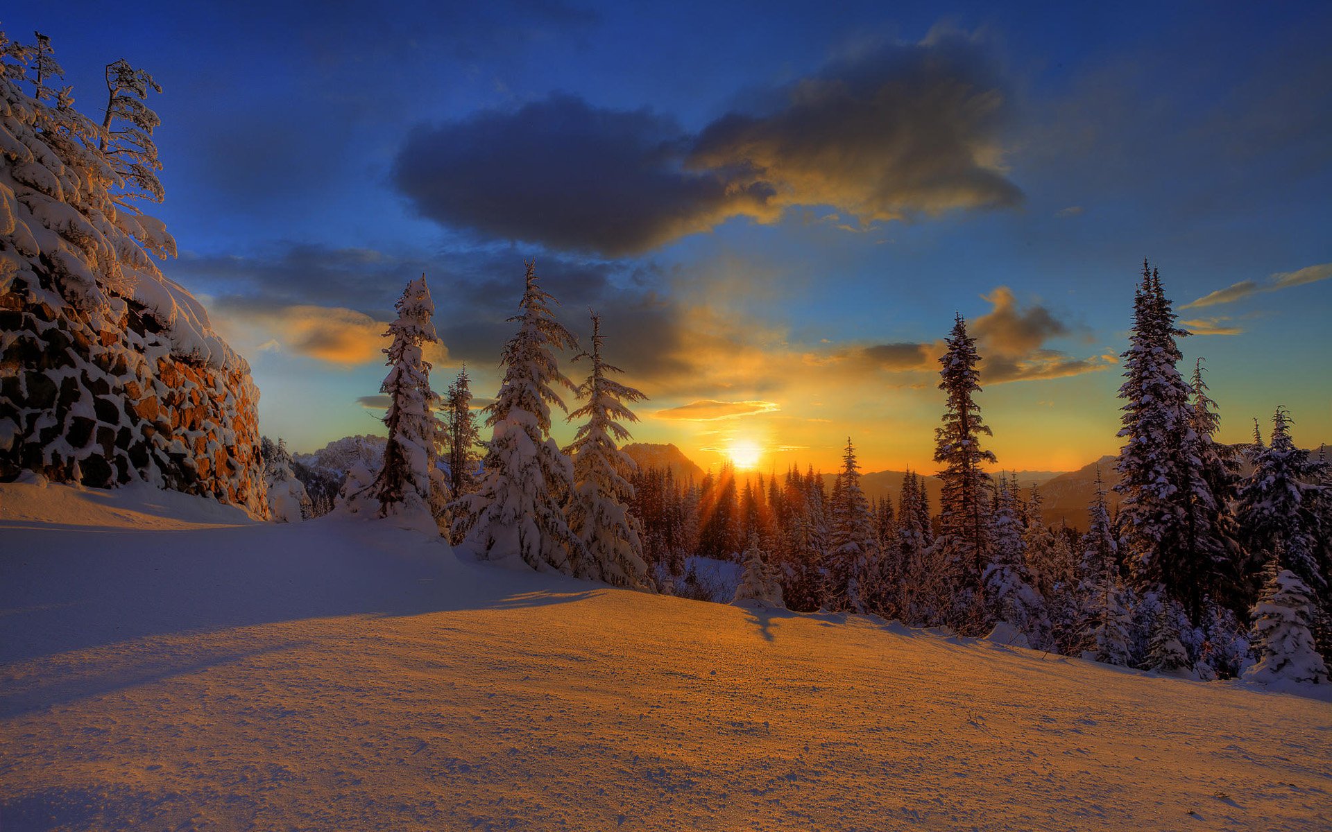 HD desktop wallpaper featuring a breathtaking sunset over a snowy, pine-forested landscape with golden sunlight streaming through the trees. Aesthetic view enhanced by a vibrant sky and softly glowing clouds.
