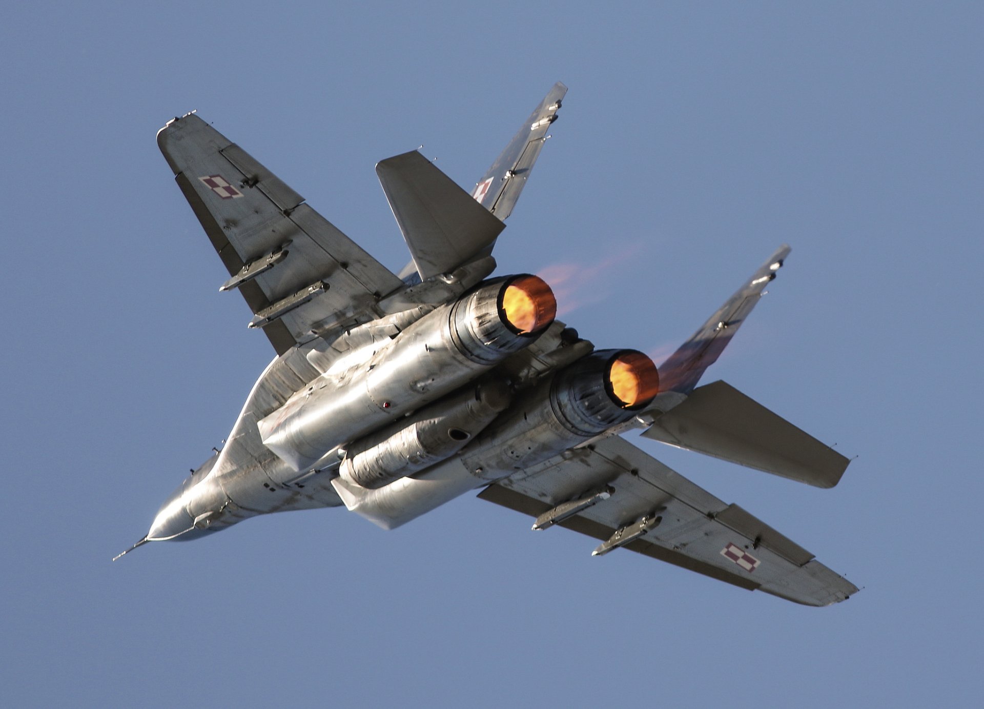 Mikoyan MiG-29 jet fighter warplane in flight with afterburners engaged, captured in high definition against a clear blue sky.