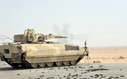 HD PC desktop wallpaper: military tan Puma IFV (infantry fighting vehicle) parked on desert asphalt, spent shell casings scattered under a clear sky.
