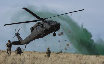 Military Sikorsky UH-60 Black Hawk helicopter in flight over a field with soldiers nearby, captured in high definition for a PC desktop wallpaper and background.