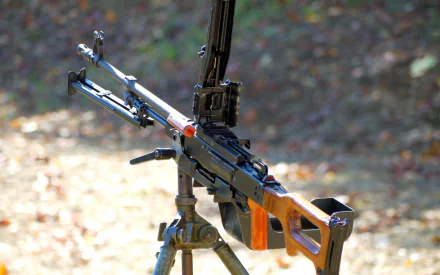 A high-definition desktop wallpaper featuring a close-up of a machine gun, highlighting its design and structure against a blurred outdoor background.
