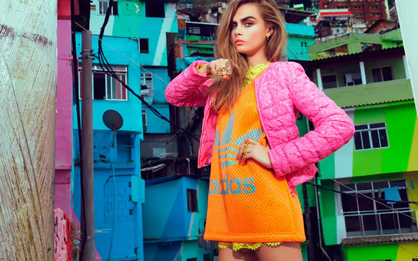 A vibrant HD wallpaper featuring Cara Delevingne in bold, colorful attire, set against a backdrop of brightly painted buildings, capturing a lively urban aesthetic.