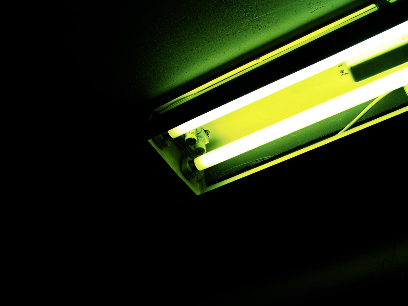 HD desktop wallpaper featuring a close-up of a glowing fluorescent light bulb in a dark environment, highlighting its man-made design and vibrant greenish-yellow illumination.