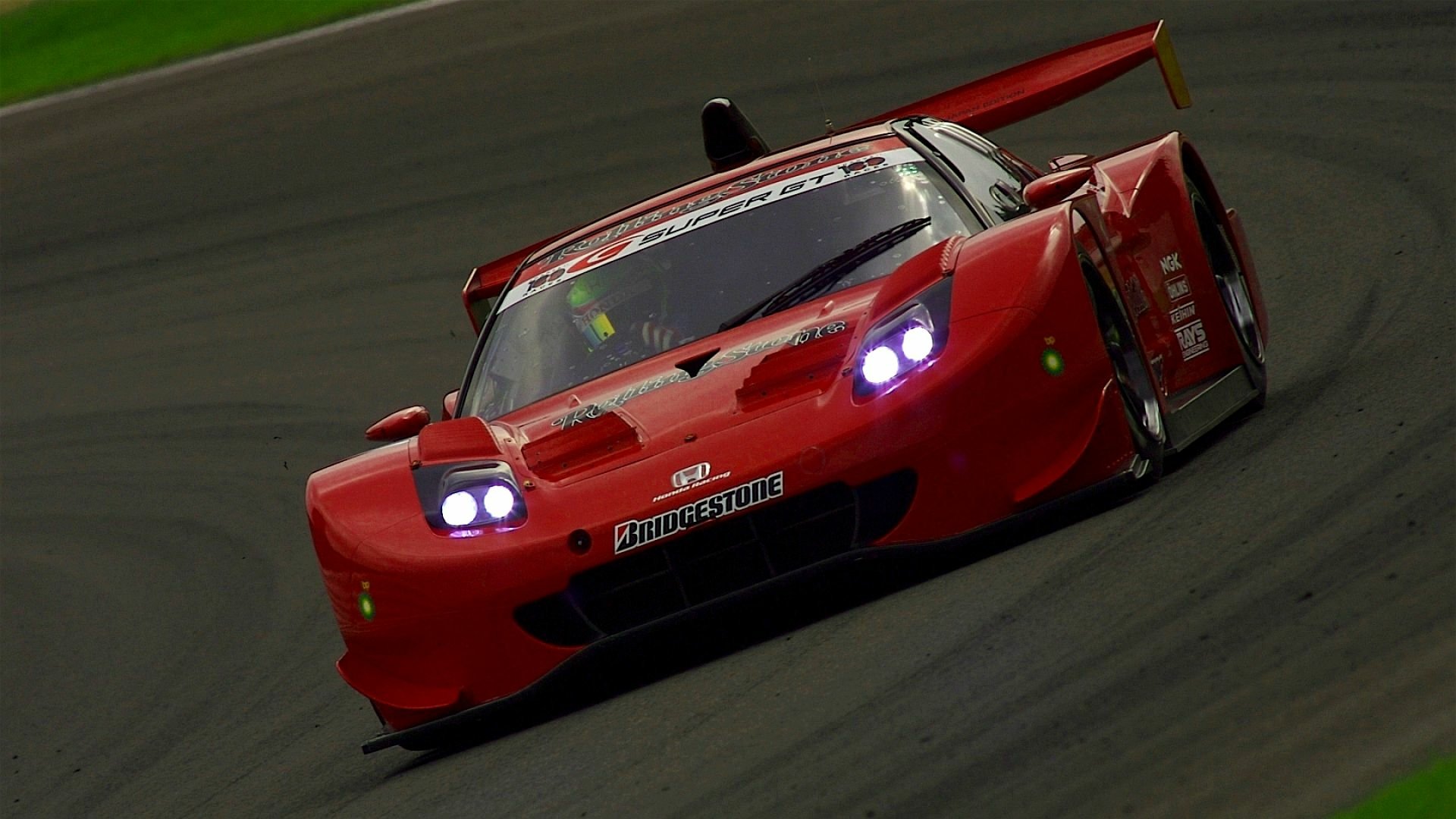 Red Honda NSX race vehicle ripping around a track, headlights aglow — HD PC desktop wallpaper/background.