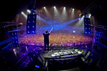 A dynamic HD wallpaper featuring Hardwell on stage, raising his hands to an electrified crowd, illuminated by vibrant lights and vibrant energy of the music scene.