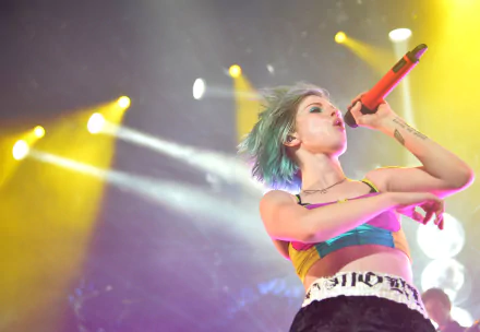 HD PC desktop wallpaper: female rock singer with short dyed hair singing into a red microphone onstage amid colorful concert lights — energetic music performance background.