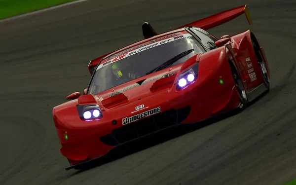 Red Honda NSX race vehicle ripping around a track, headlights aglow — HD PC desktop wallpaper/background.