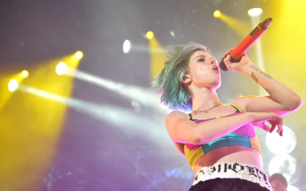 HD PC desktop wallpaper: female rock singer with short dyed hair singing into a red microphone onstage amid colorful concert lights — energetic music performance background.