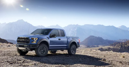 4K Ultra HD desktop wallpaper featuring a blue Ford Raptor truck parked on rocky terrain with mountains and a clear sky in the background.