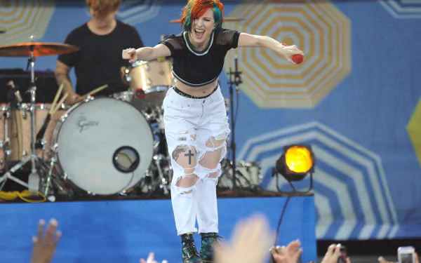 Music-themed 4K Ultra HD PC desktop wallpaper: orange-haired female rock singer leaping onstage, drummer behind her and cheering crowd in foreground.