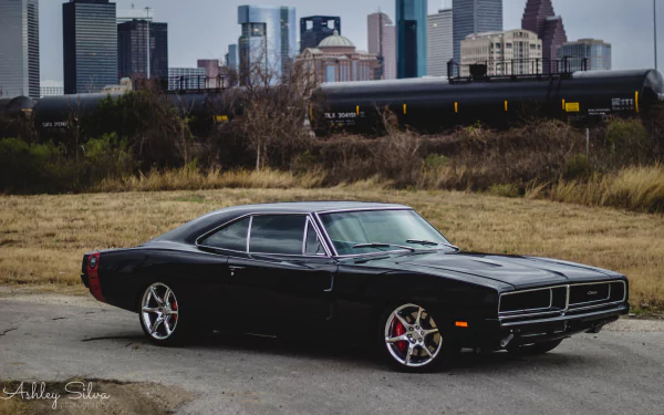 A sleek black Dodge Charger parked against a city skyline, showcasing its sporty design. This HD desktop wallpaper captures the vehicle's bold presence in an urban setting.