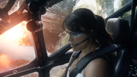 Trudy Chacón, portrayed by Michelle Rodriguez, pilots a vehicle with determination as explosions erupt in the background, showcasing her brown hair and distinctive necklace.