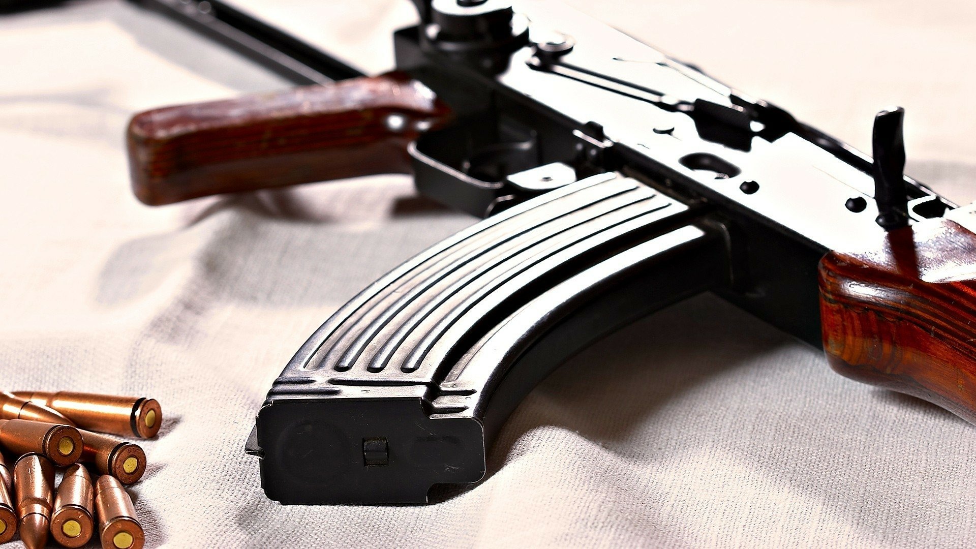 Close-up of an AK-47 with a magazine and bullets on a neutral background, showcasing the weapon's intricate details in high definition, suitable as a desktop wallpaper or background.