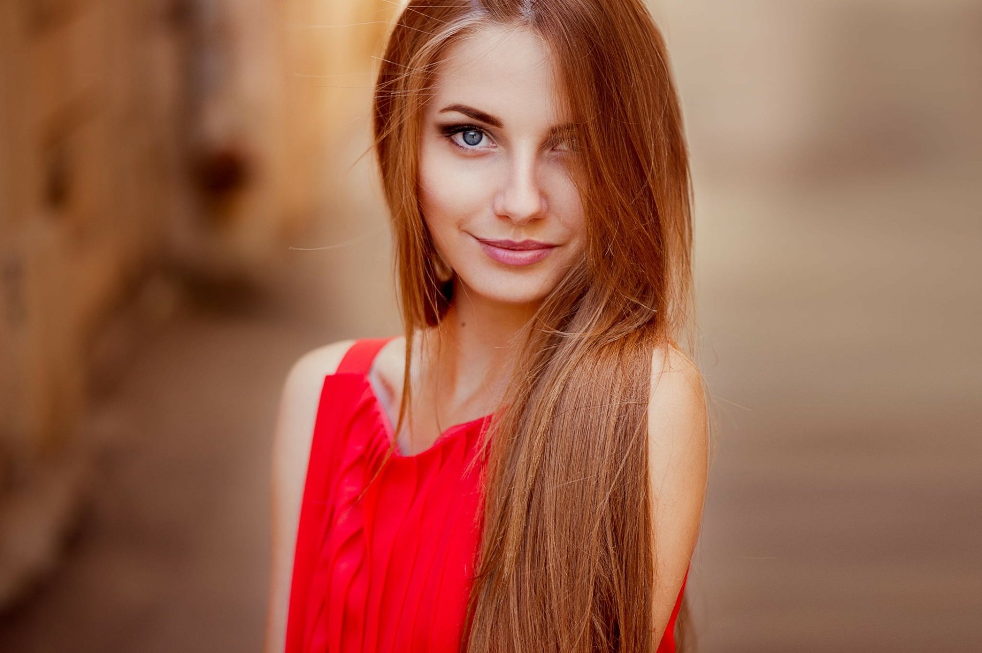 HD desktop wallpaper featuring a woman with long hair and blue eyes, wearing a red top, captured in a soft-focus background.