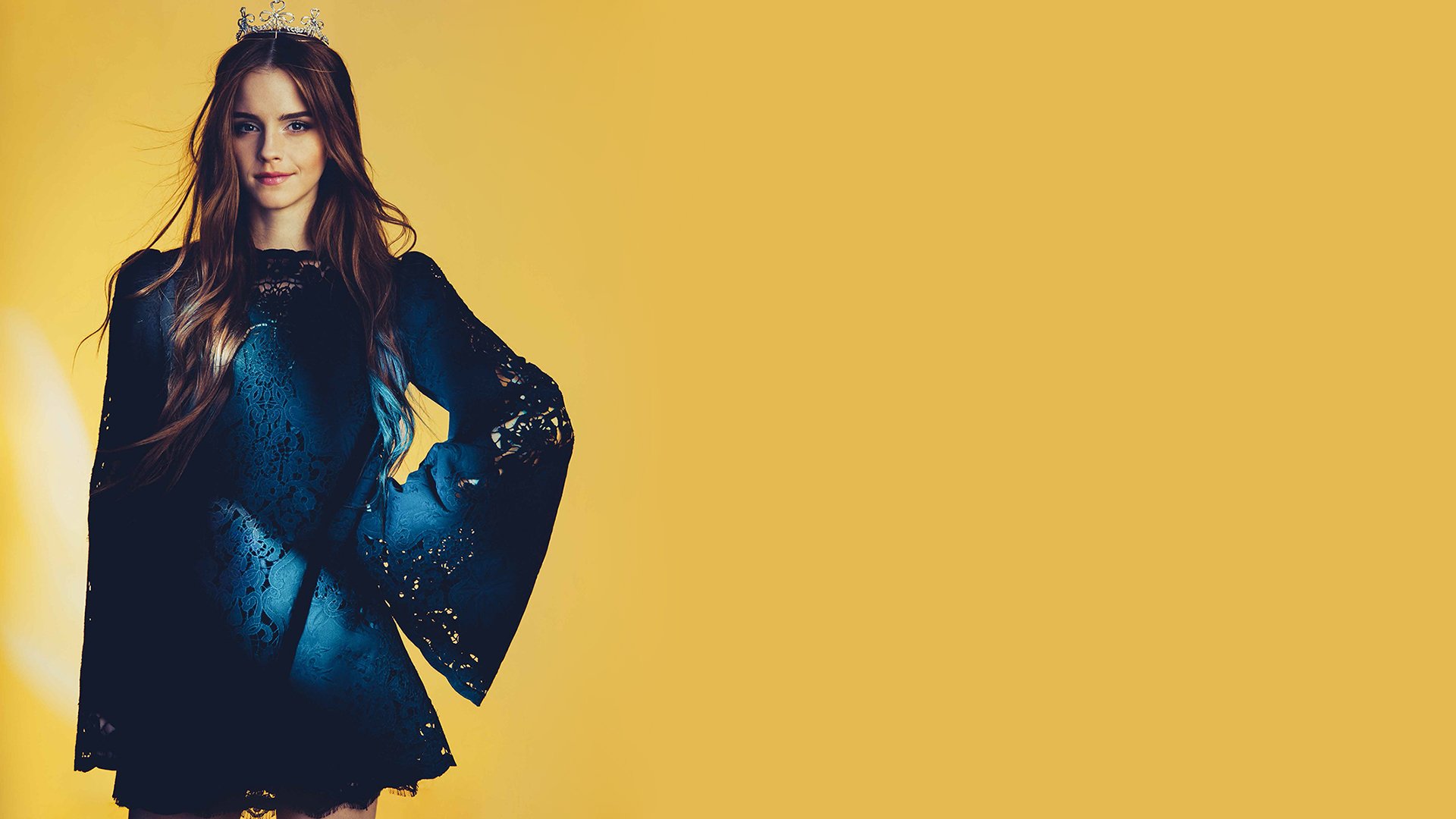 Emma Watson poses confidently in a stylish, bell-sleeved black dress against a vibrant yellow background, making this an eye-catching HD desktop wallpaper.