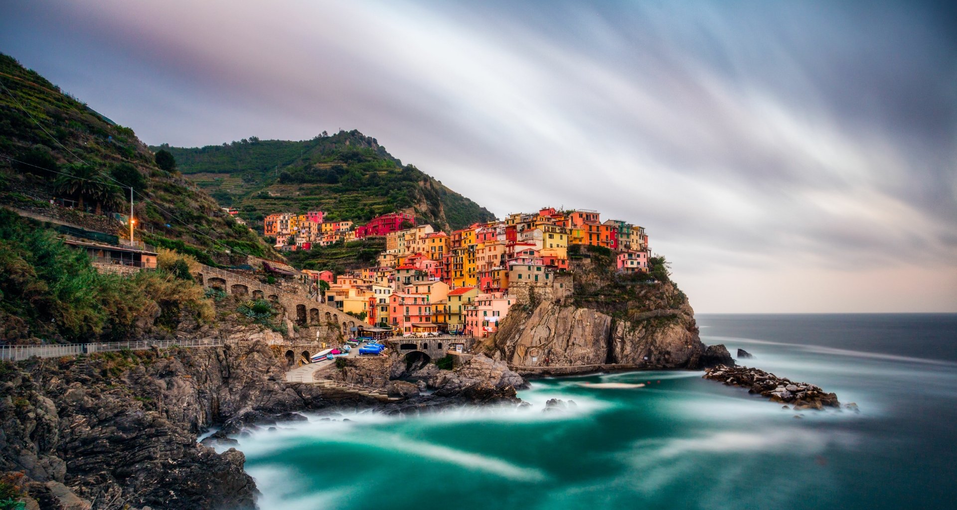 Man-made colorful cliffside village of Manarola at sunset, sweeping coastal cliffs and turquoise sea in a 5K Ultra HD PC desktop wallpaper/background.