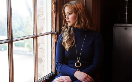 A candid portrait of celebrity Jennifer Lawrence, sitting by a window in a stylish outfit, captured in a warm, inviting setting. This HD image serves as an attractive desktop wallpaper.