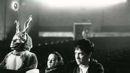 Black and white HD desktop wallpaper featuring Jena Malone and Jake Gyllenhaal from the movie Donnie Darko, with the iconic rabbit figure in the background.