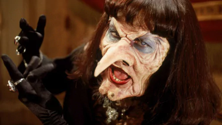 HD PC desktop wallpaper: close-up of a snarling, grotesque witch from the movie The Witches (1990) with a hooked nose, heavy makeup and gloved hands.