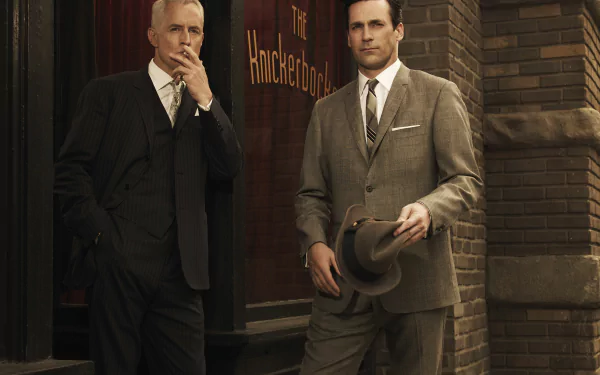 2K Quad HD Mad Men TV show desktop wallpaper: two sharply dressed 1960s men in suits stand outside an office building, one holding a hat.