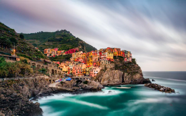 Man-made colorful cliffside village of Manarola at sunset, sweeping coastal cliffs and turquoise sea in a 5K Ultra HD PC desktop wallpaper/background.