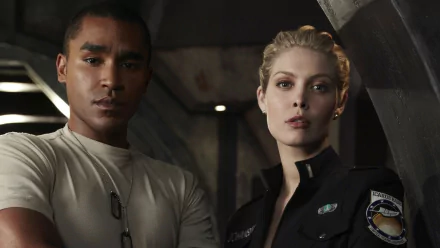 HD PC desktop wallpaper and background showing two crew members from the TV show Stargate Universe standing in a dim ship corridor.