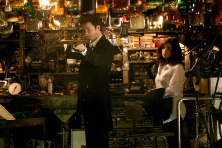 HD wallpaper featuring Rachel Weisz and Keanu Reeves in a scene from the movie Constantine, set in a cluttered room with hanging glass and various objects.