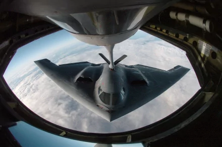 A Northrop Grumman B-2 Spirit stealth aircraft is shown in flight, captured from above as it receives fuel mid-air. The HD image serves as a striking military-themed desktop wallpaper.