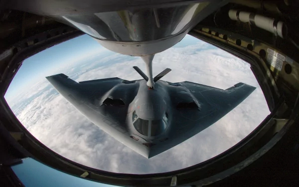 A Northrop Grumman B-2 Spirit stealth aircraft is shown in flight, captured from above as it receives fuel mid-air. The HD image serves as a striking military-themed desktop wallpaper.