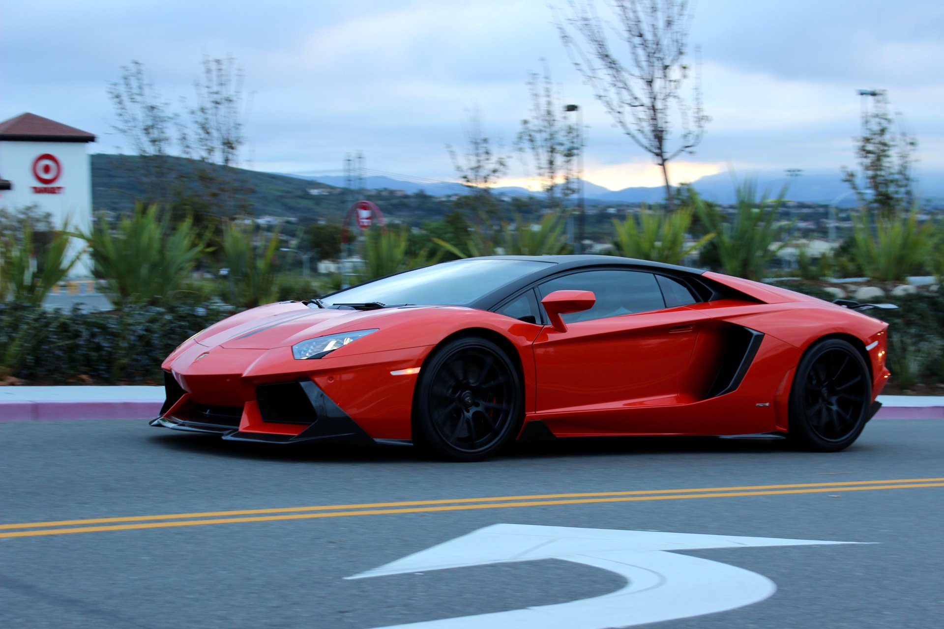 Red Lamborghini Aventador sports car on a street with trees and hills in the background, captured in 4K Ultra HD for PC desktop wallpaper.