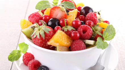 Vibrant HD desktop wallpaper featuring a bowl of fresh mixed fruit including strawberries, raspberries, blueberries, orange slices, and mint leaves on a light background.