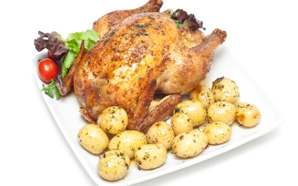 4K Ultra HD PC desktop wallpaper featuring a roasted chicken with seasoned baby potatoes and fresh greens on a white plate.