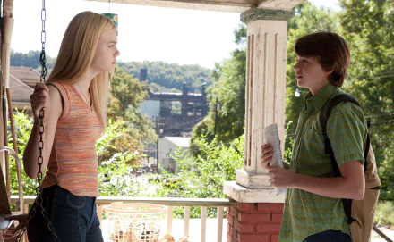 HD desktop wallpaper featuring Joel Courtney and Elle Fanning in a scene from the movie Super 8, set on a porch with lush greenery and a distant bridge in the background.