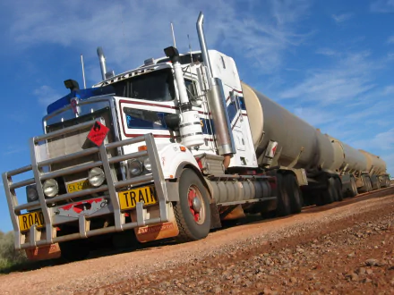 HD desktop wallpaper featuring a Kenworth road train truck on a dirt road under a blue sky.