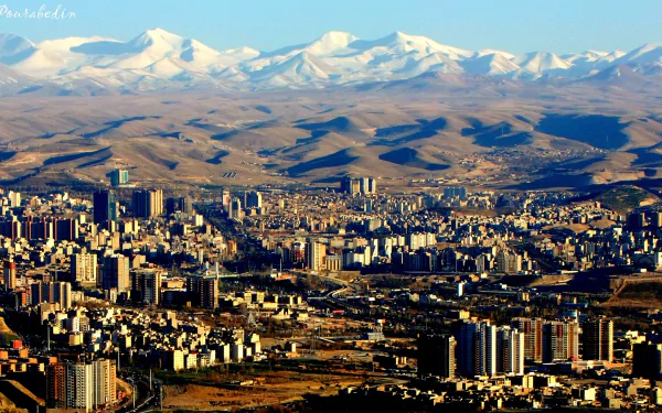 HD desktop wallpaper showcasing the man-made urban landscape of Tabriz with a backdrop of snow-capped mountains under a clear sky.