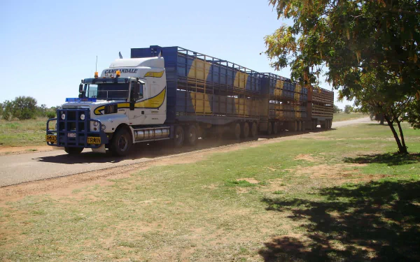 HD desktop wallpaper showing an Iveco road train driving on a rural dirt road under a clear sky with trees nearby.